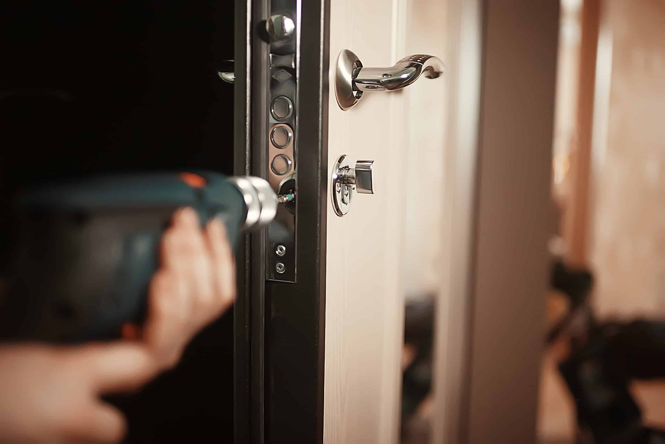 Main tenant une perceuse électrique pour installer une serrure multipoints sur une porte moderne. Travaux de sécurité résidentielle.