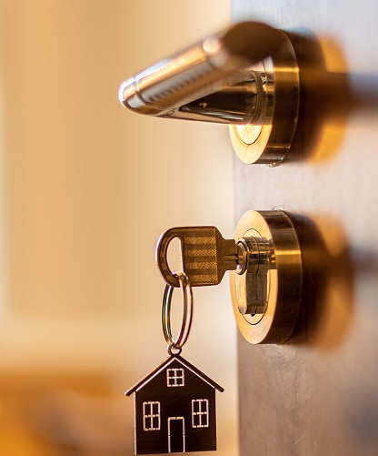 Clé insérée dans une serrure de porte en bois sombre, avec un porte-clés en forme de maison. Symbole d'achat ou d'accès au logement.