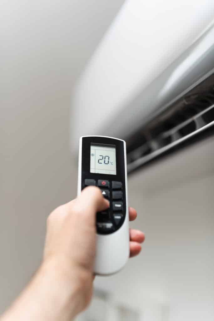 Main réglant la climatisation à 20°C avec une télécommande affichant un flocon de neige, mode refroidissement activé.